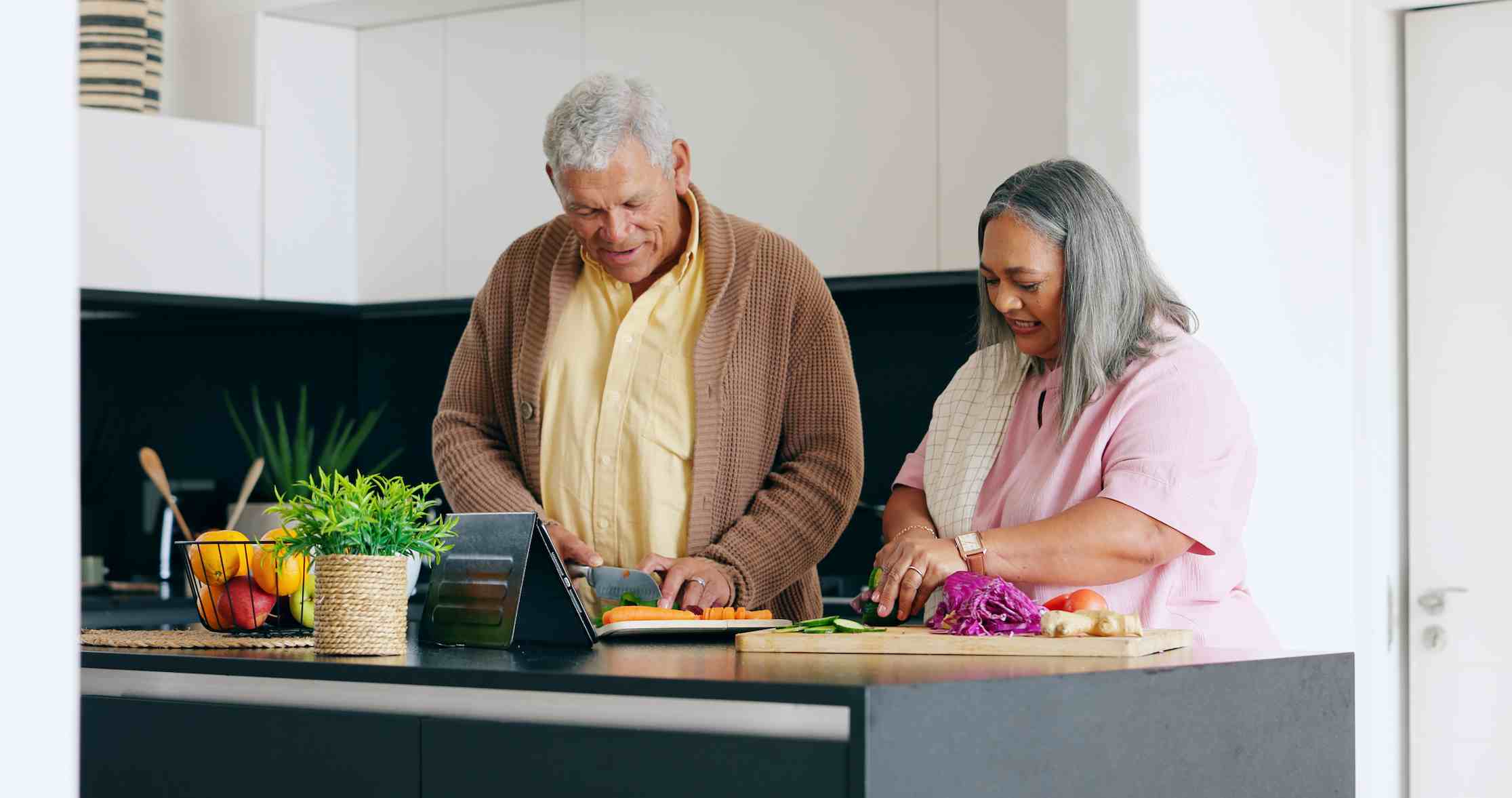 elderly couple cutting vegetables and cooking while smiling
