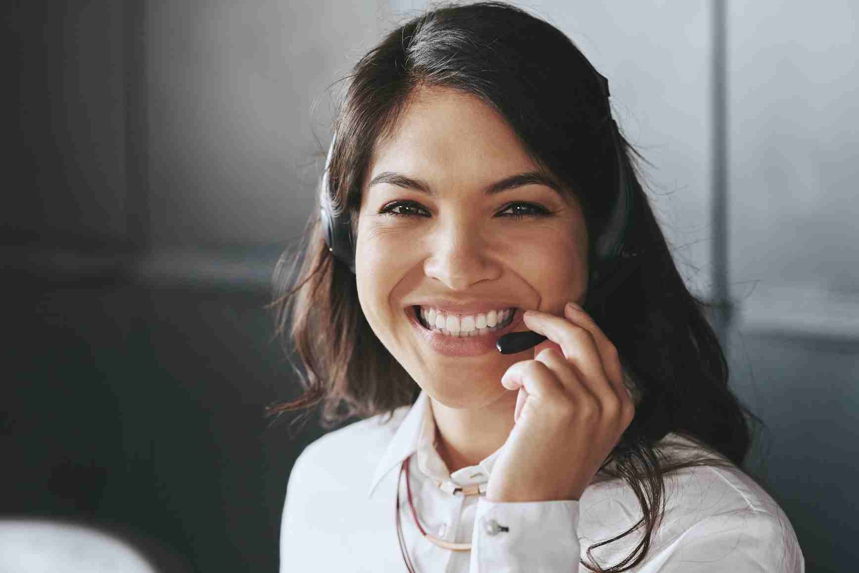 A young woman who is a medicare guide with a phone headset smiling while helping seniors over the phone